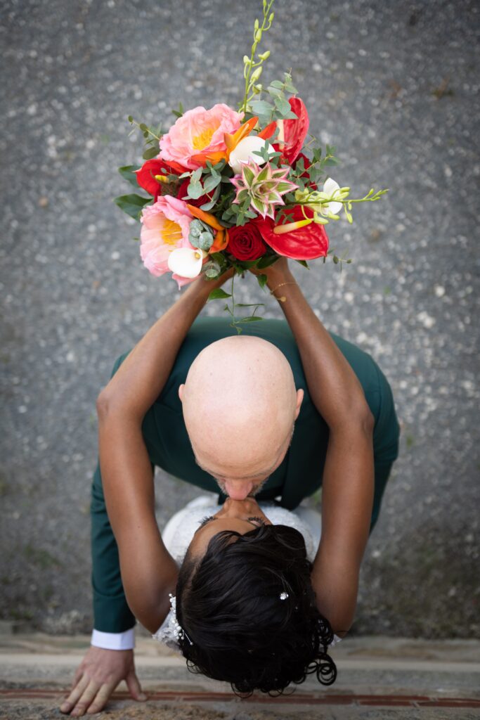 Mariage de Valéry et Olivier au parc des Capucins à Coulommiers, baiser vu du dessus avec bouquet coloré en premier plan.