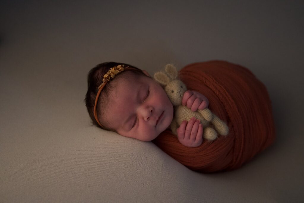 Séance photo naissance de Gabriela au home studio à Meaux, tenant un petit lapin en laine dans une couverture orange.