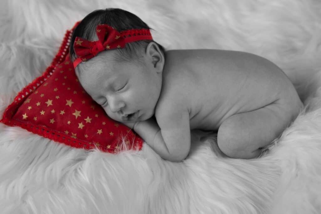 Shooting photo naissance de Jade au home studio à Meaux, posée sur une couverture douce avec un bandeau fleuri rouge.