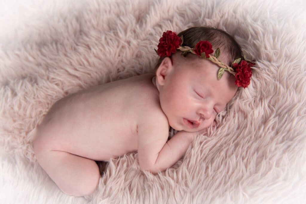 Shooting photo naissance Jade au home studio à Meaux, posée sur un coussin rouge orné d’un bandeau assorti, dans une ambiance douce et élégante.