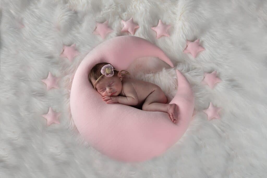 Shooting photo naissance Jade au home studio à Meaux, endormie sur un coussin en forme de lune rose entourée d’étoiles