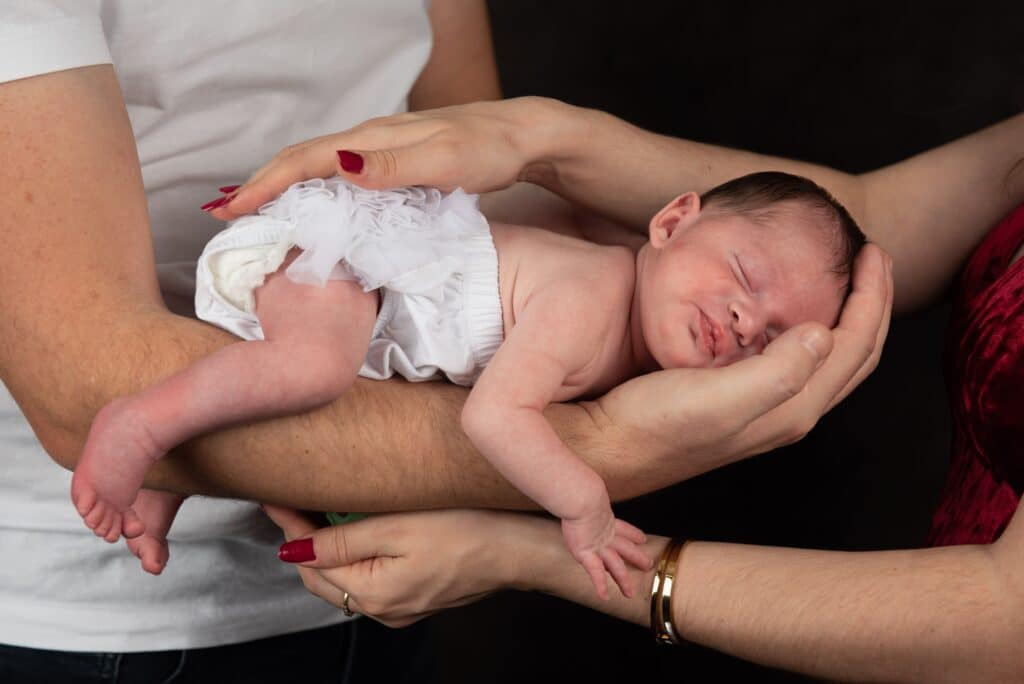 Shooting photo naissance Jade au home studio à Meaux, tenue délicatement par ses parents, symbolisant l’amour familial.