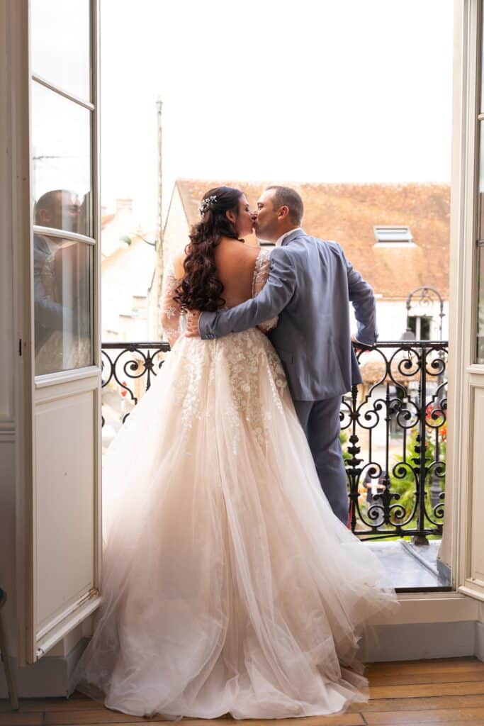 Shirley et Jonathan s’embrassant sur un balcon lumineux pendant leur réception à Saint, photographiés par Arnaud-M Photographe lors du mariage de Shirley et Jonathan à Coulommiers.